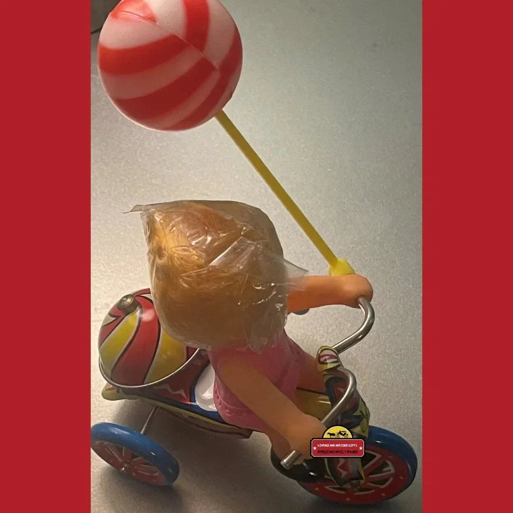 Vintage tin wind toy with a plastic figure on a tricycle holding a balloon