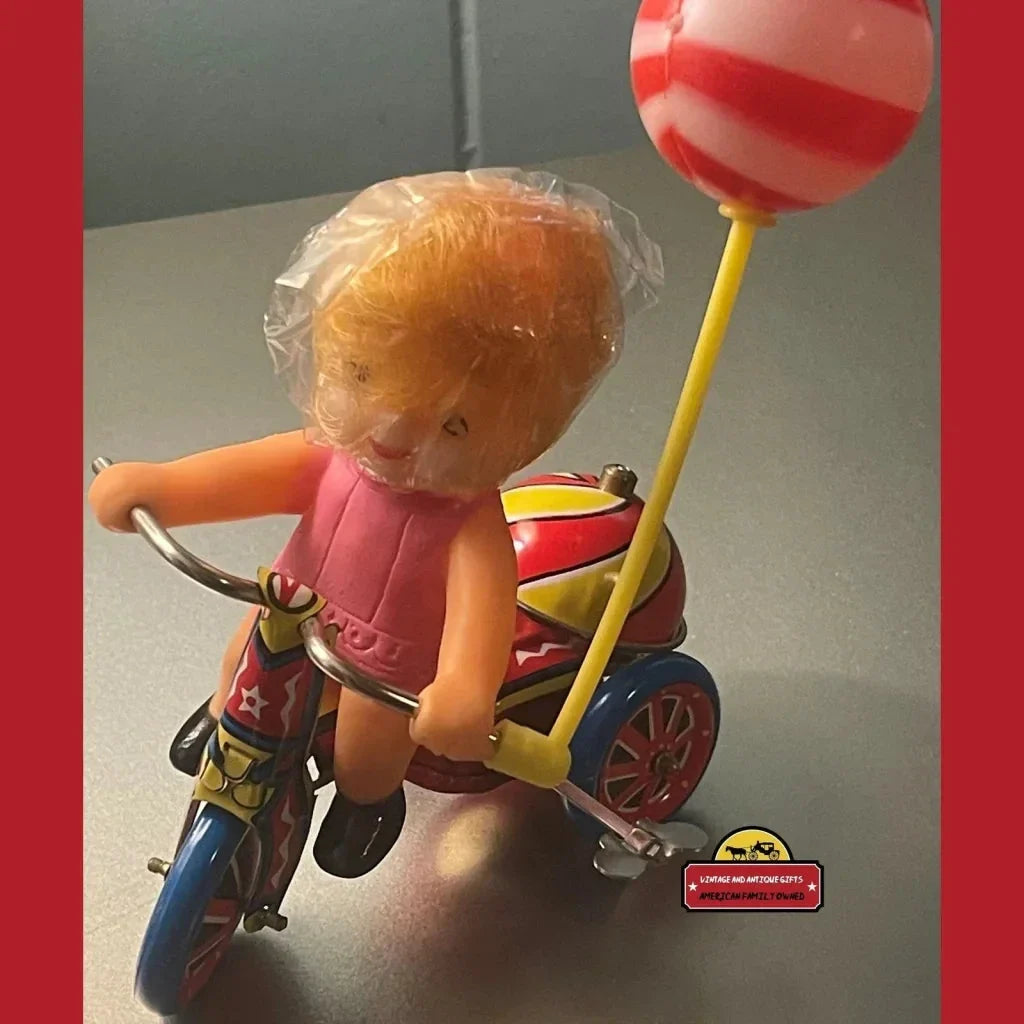 Vintage plastic doll on a colorful toy tricycle with balloon in Nostalgic Vintage Tin Wind