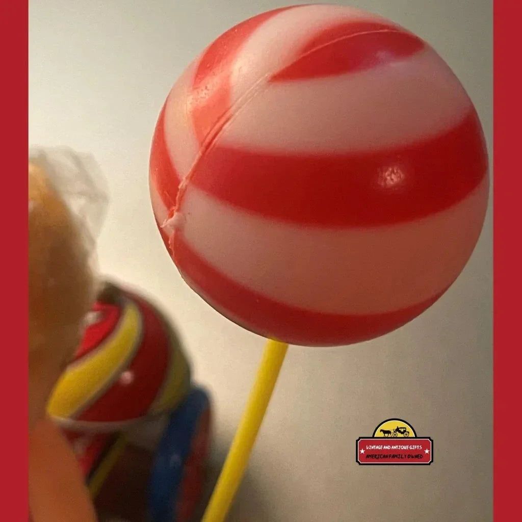 Red and white striped lollipop on a yellow stick beside Vintage Tin Wind Up Tricycle Toy