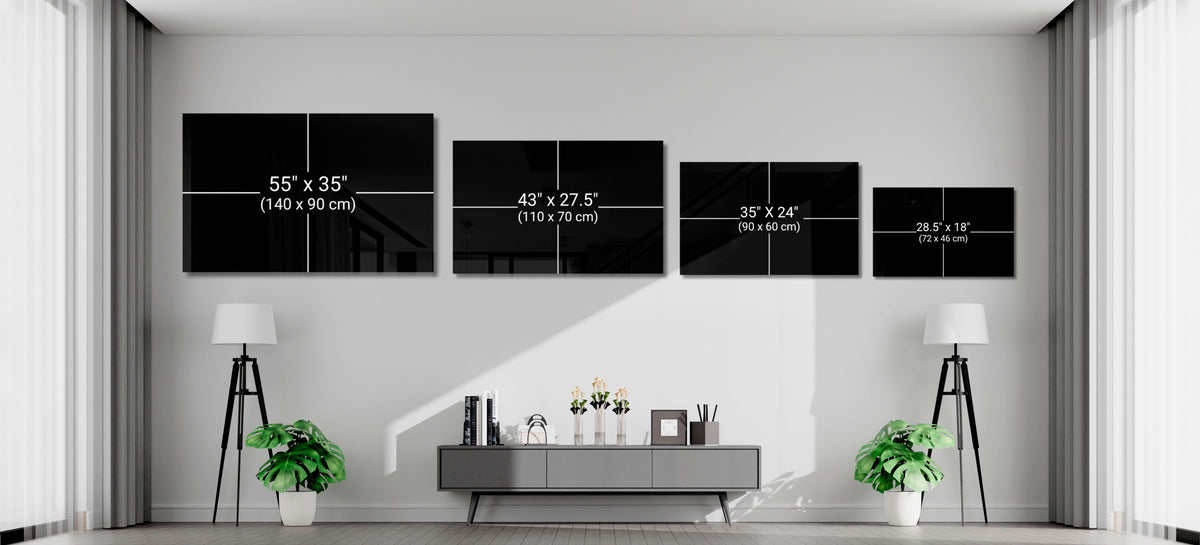 Four black glass wall art panels of decreasing sizes displaying size dimensions in inches and centimeters, hung above a gray console table in a modern living room.