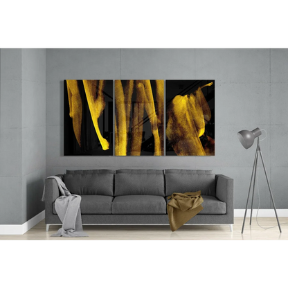 Three-panel golden banana leaf glass wall art on black canvas above gray sofa