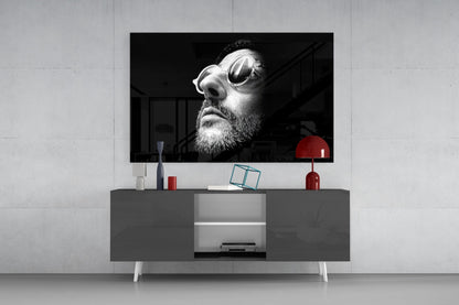 Black and white portrait of bearded man wearing oval sunglasses displayed on wall-mounted television above gray console table with red lamp and accessories.