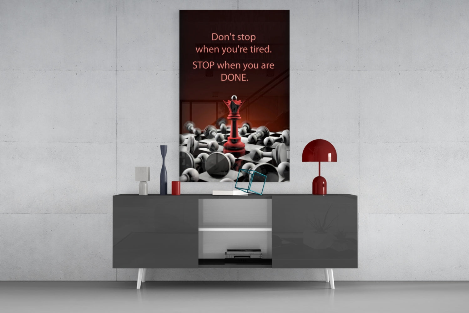 Motivational glass wall art with red chess piece and gray spheres displayed above gray console table with red lamp and decorative accessories.