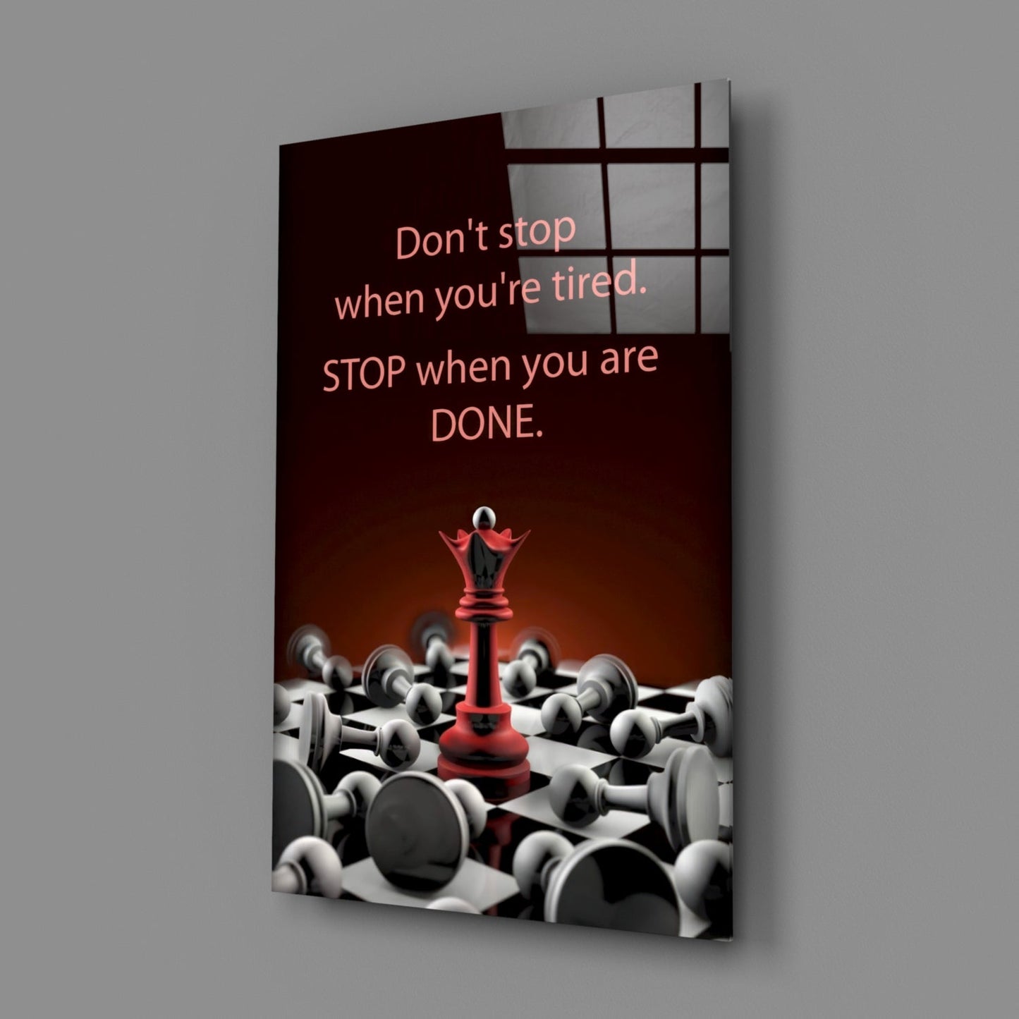 Angled view of glass wall art displaying motivational quote with red chess queen surrounded by white pawns on dark background.