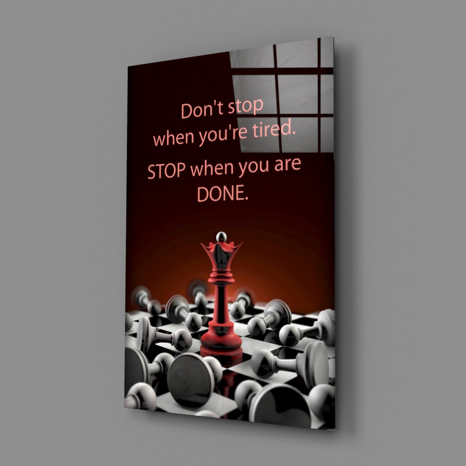 Angled view of glass wall art displaying motivational quote with red chess queen surrounded by white pawns on dark background.