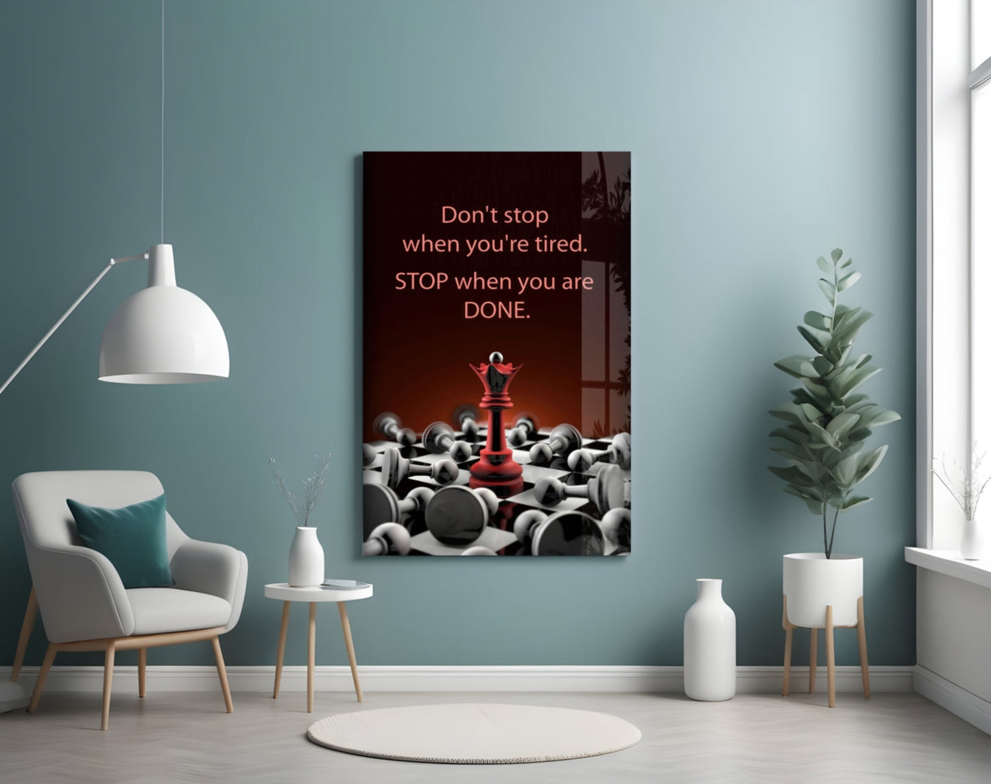 Motivational glass wall art with red text and chess piece imagery displayed in a minimalist room with teal walls, white furniture, and potted plants.