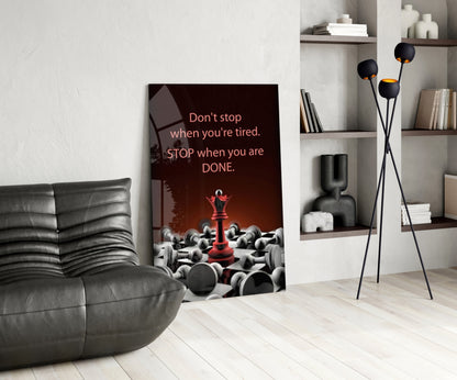Motivational glass wall art displayed in modern living room with gray sofa, showing chess pieces and red queen with inspirational text.