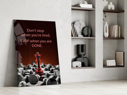 Glass wall art leaning against white wall displaying red chess queen among fallen pieces with motivational text on dark background.