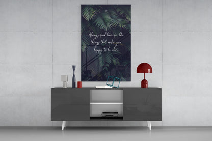 Dark glass wall art with fern leaves and white script text "Always find time for the things that make you happy to be alive" displayed above a grey media console.