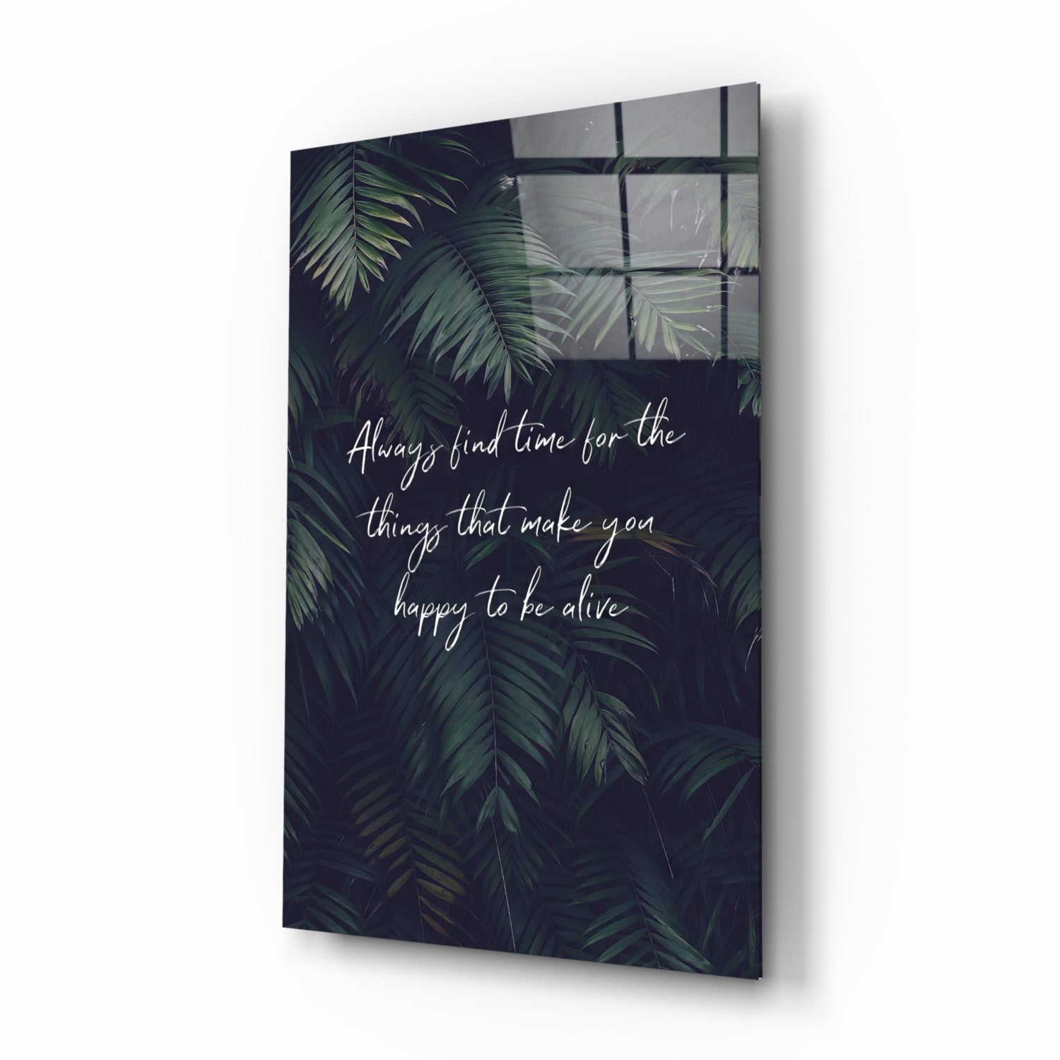 Angled view of glass wall art with dark foliage background and white script text about finding time for happiness.