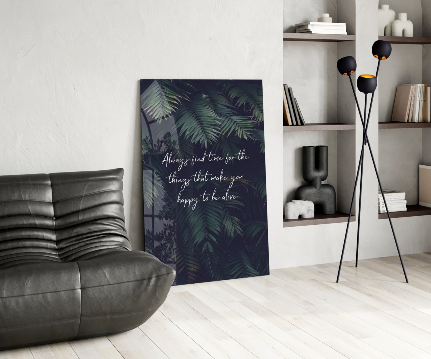 Dark botanical glass wall art with white inspirational text displayed in modern living room beside leather chair and shelving unit.