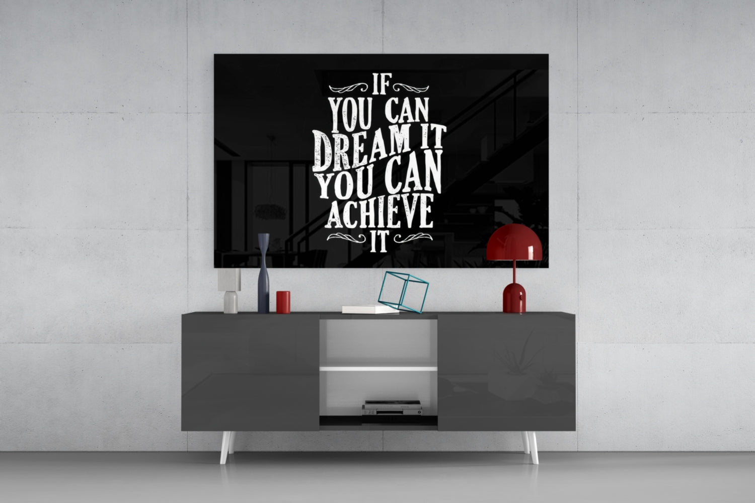 Black glass wall art with white inspirational text mounted above gray media console in modern living room setting with red lamp and decorative accessories.