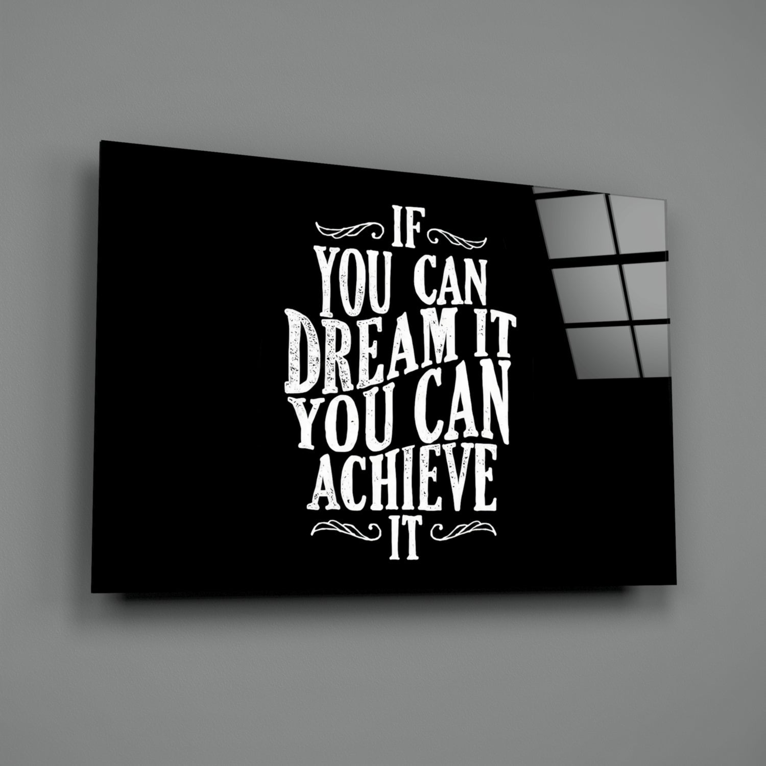 Black glass wall art panel displaying white motivational text "If You Can Dream It You Can Achieve It" with decorative flourishes, angled view showing depth.