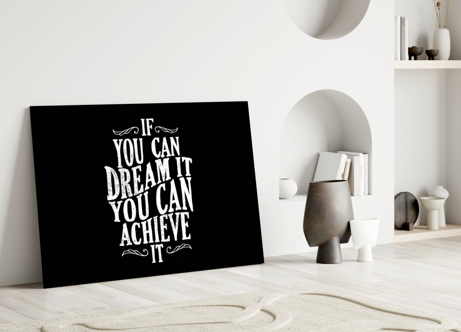Black glass wall art with white motivational text leaning against white wall in minimalist room setting.