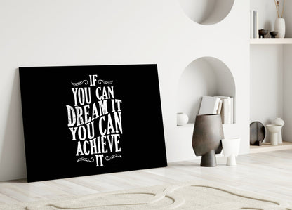 Black glass wall art with white motivational text leaning against white wall in minimalist room setting.