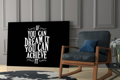 Black glass wall art with white inspirational text displayed in a modern living room beside a wooden chair with blue cushions.