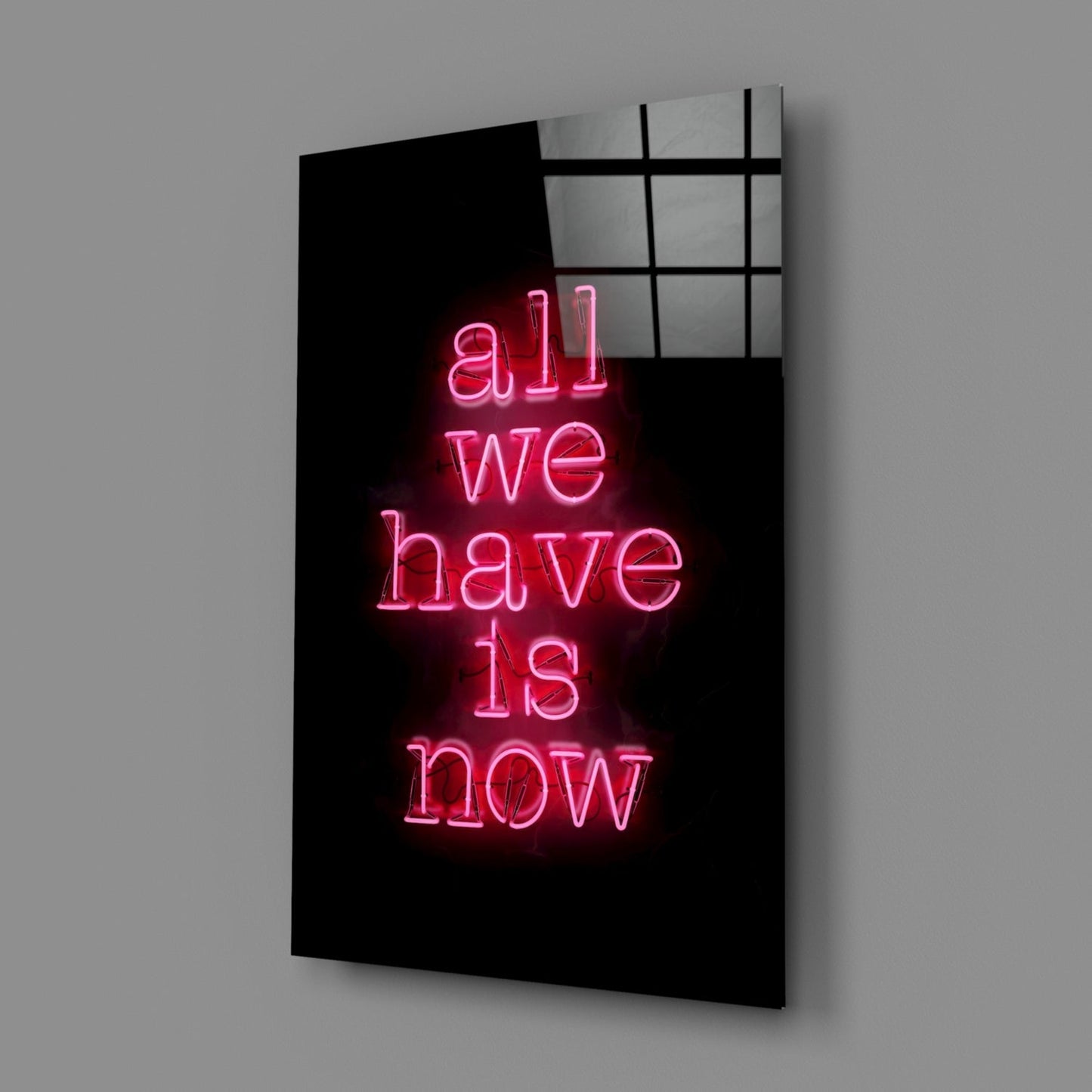 Pink neon text reading "all we have is now" on black glass panel with grid pattern overlay, angled perspective view.