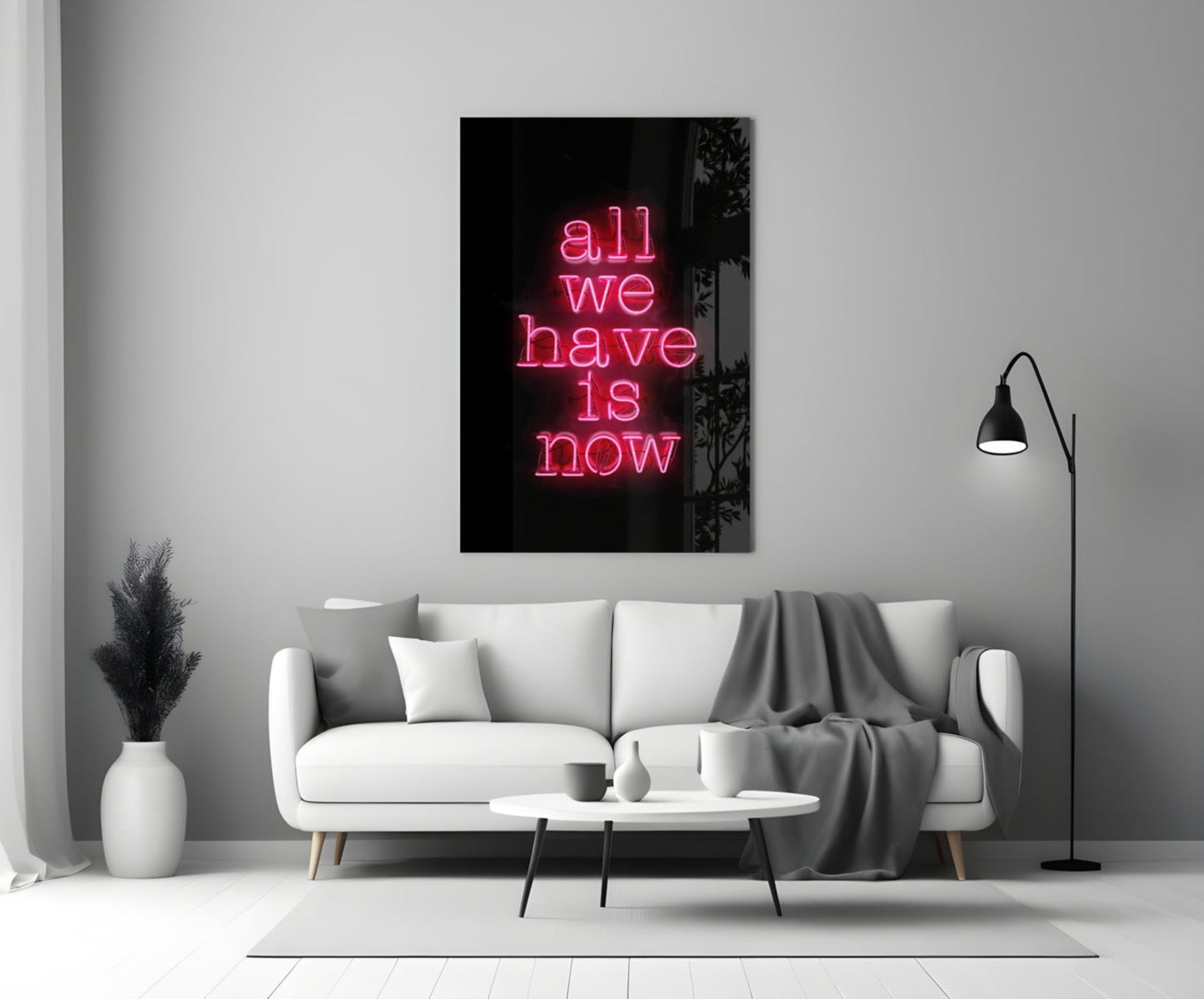 Pink neon text reading "all we have is now" on black glass mounted above white sofa in modern living room interior.
