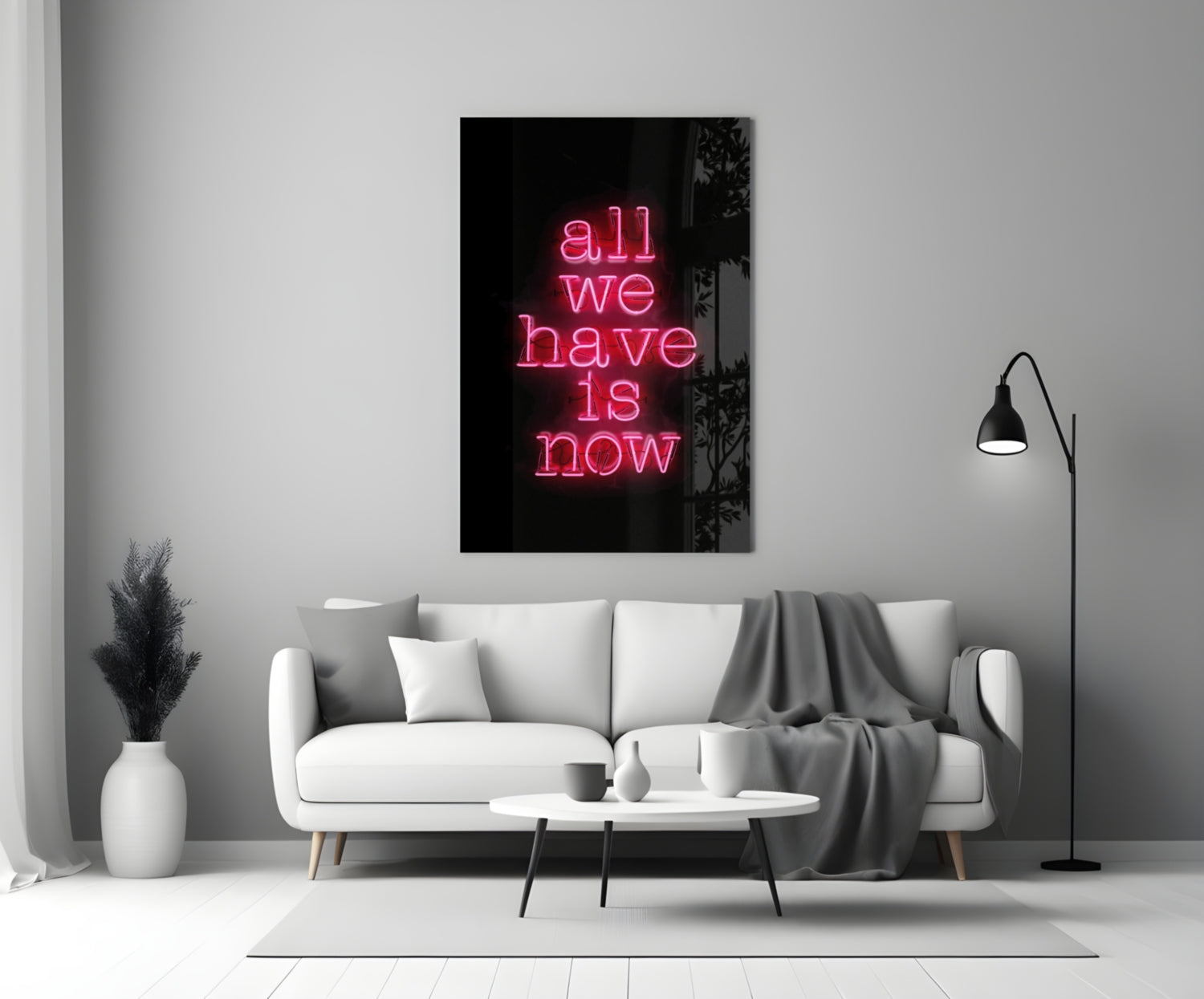 Pink neon text reading "all we have is now" on black glass mounted above white sofa in modern living room interior.