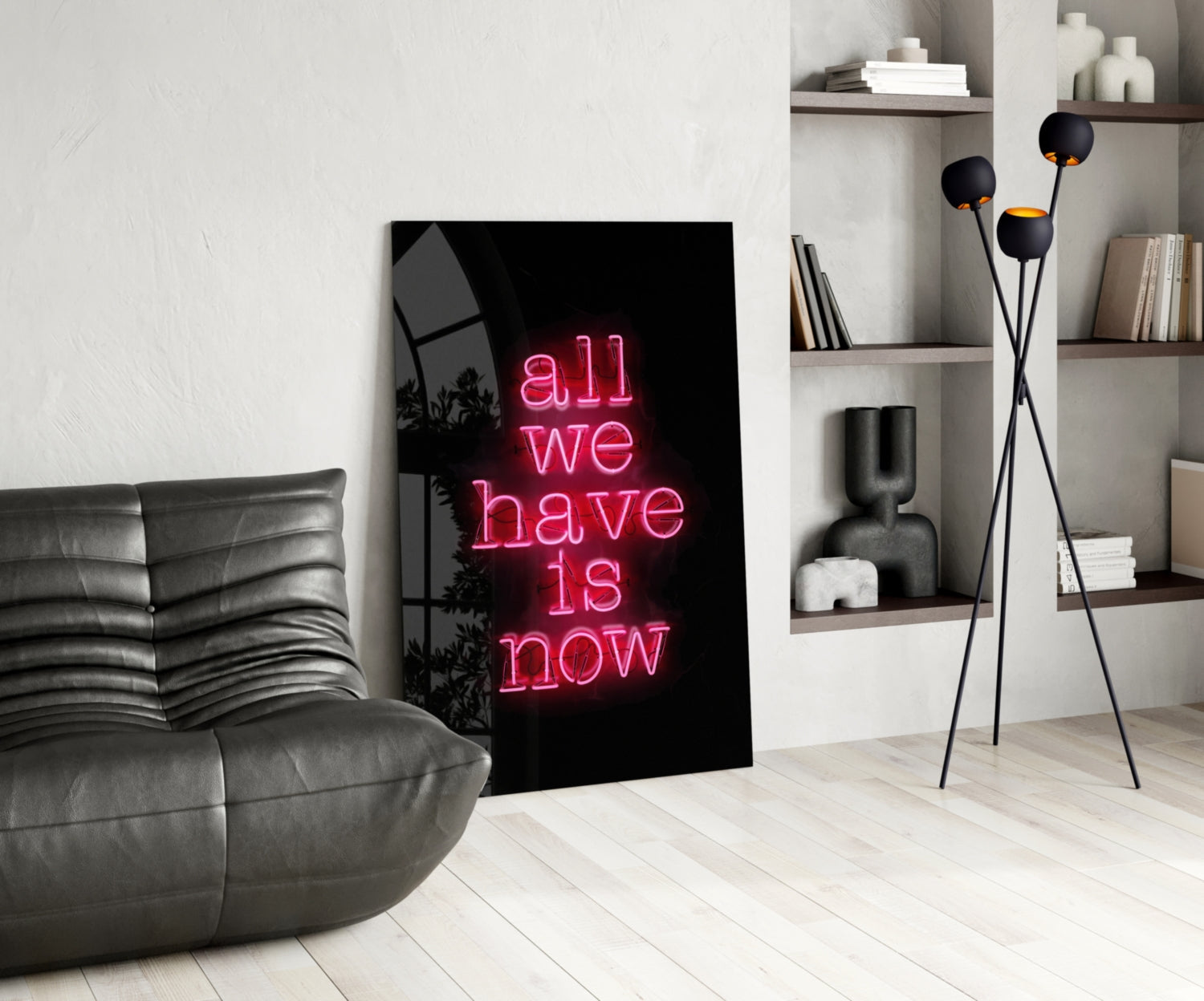 Pink neon "all we have is now" text on black glass leaning against white wall in modern living room setting.