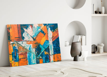 Colorful abstract glass art with orange, blue, and yellow geometric patterns leans against white wall beside decorative objects.