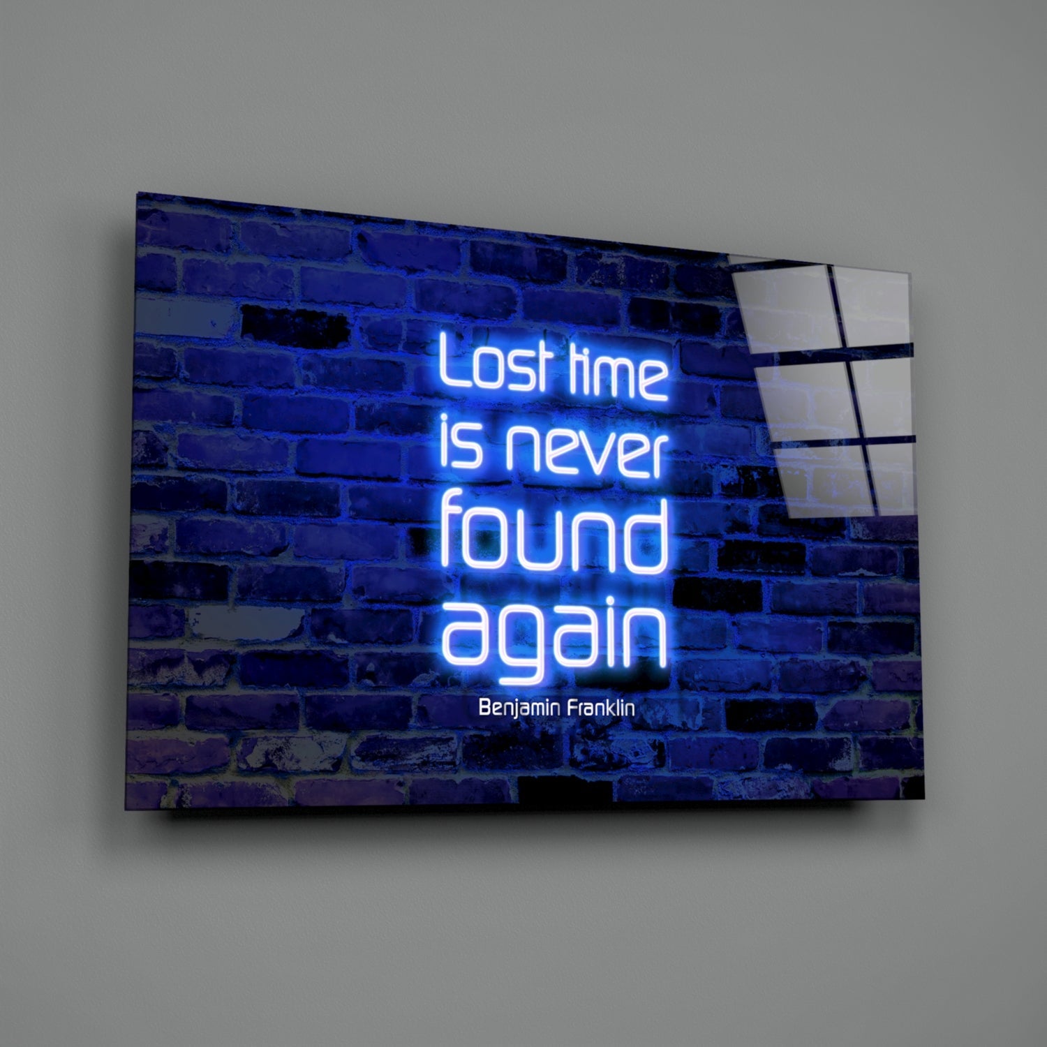 Angled view of a glass wall art panel displaying blue neon lettering reading "Lost time is never found again" with Benjamin Franklin attribution, mounted on a gray wall.