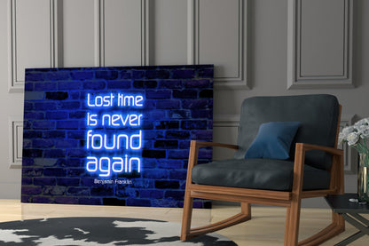 Neon blue glass wall art displaying Benjamin Franklin quote "Lost time is never found again" mounted in modern living room beside wooden chair.