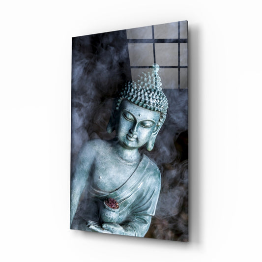 A serene Buddha statue with textured crown and draped robe against a dark smoky background, with a small red lotus flower detail on the chest, displayed as glass wall art.
