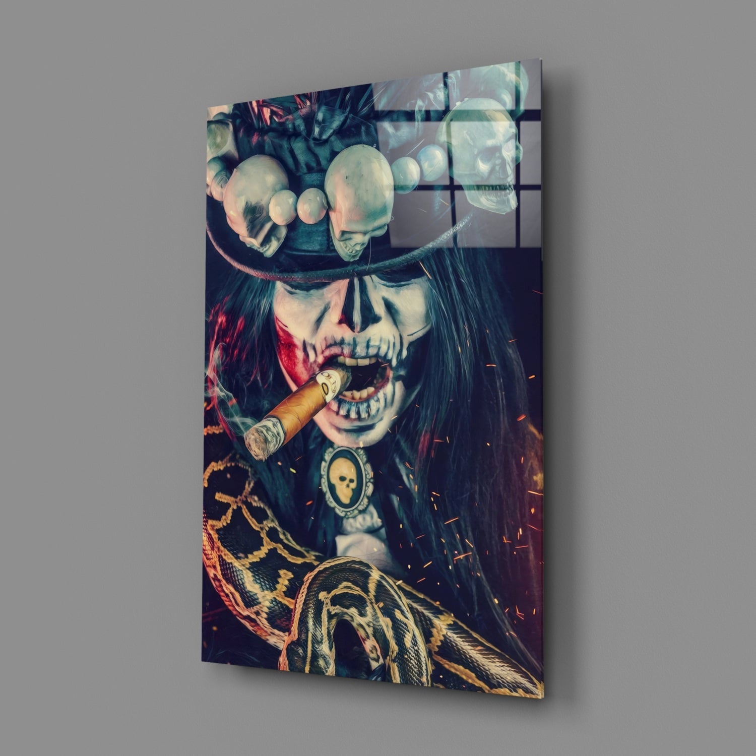 Angled view of glass wall art depicting a skull with cigar, ornate chains, and feathered details in dark tones with red and gold accents.