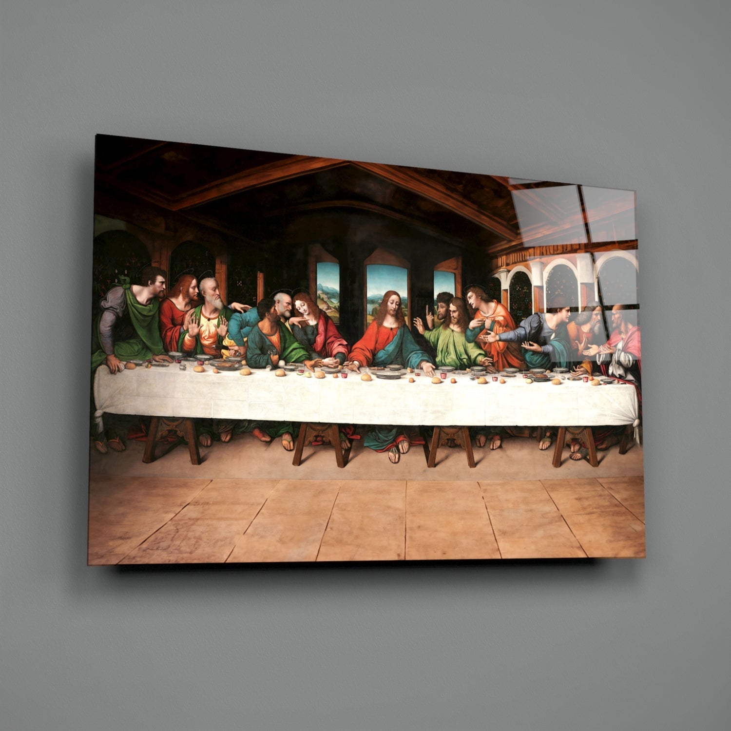 Glass wall art depicting the Last Supper scene with thirteen figures seated at a table, mounted on a gray wall.