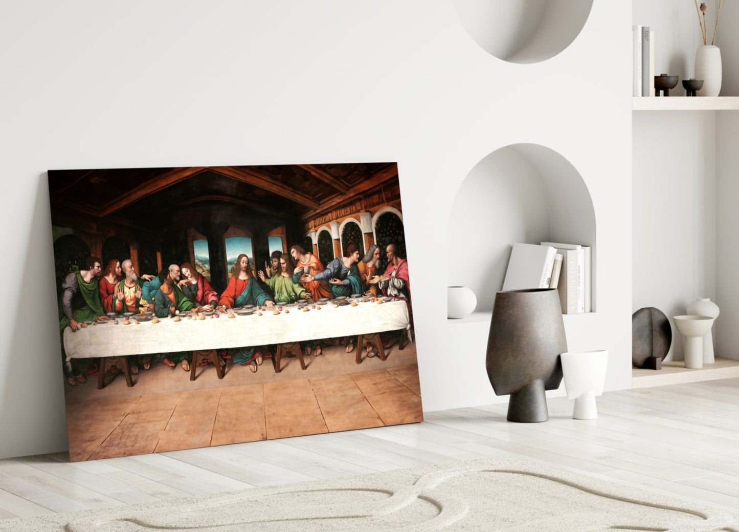 Glass wall art of Last Supper painting leaning against white wall in minimalist interior with decorative objects.