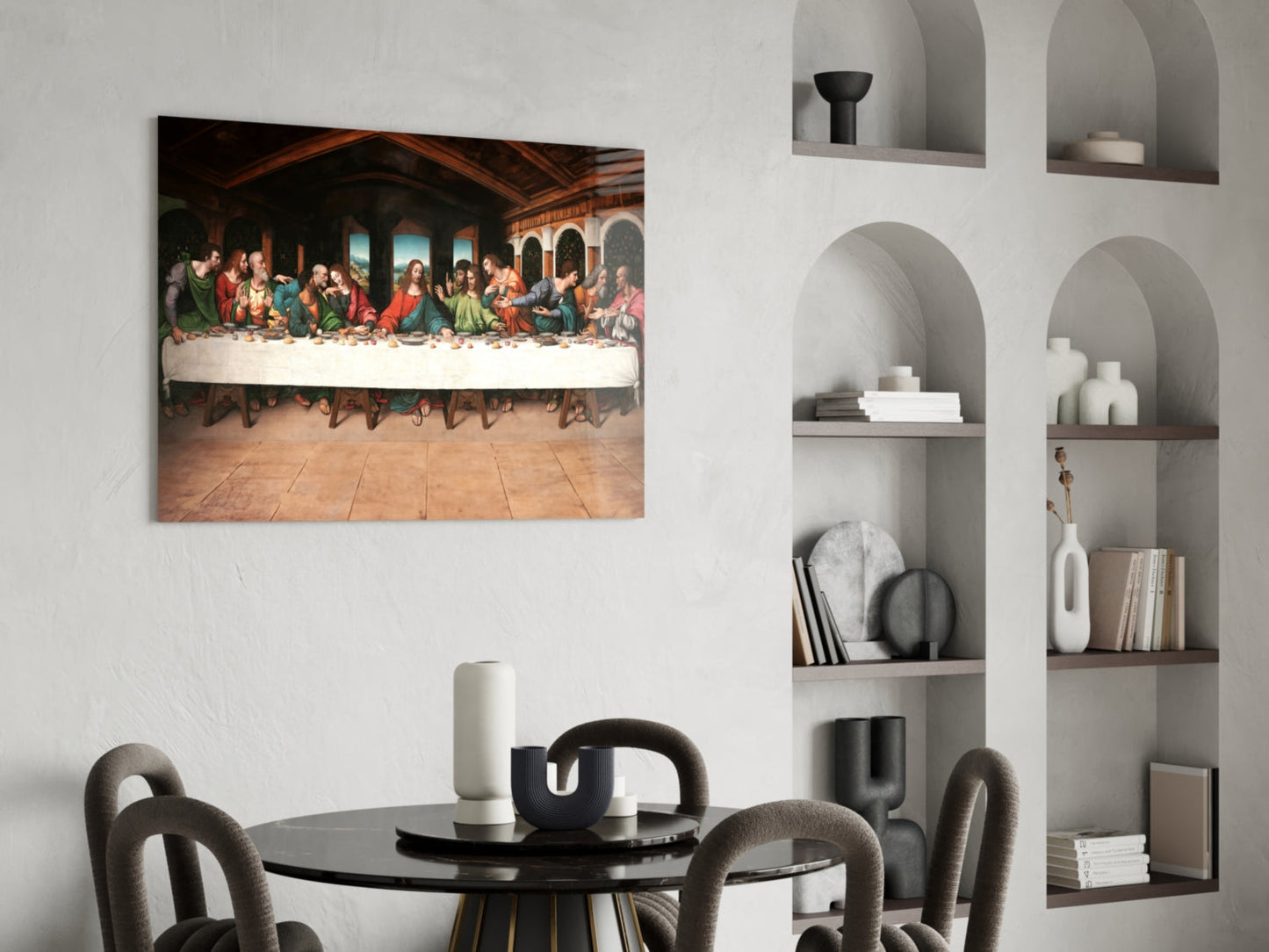 Last Supper Remastered glass wall art hanging above a black round dining table with gray upholstered chairs in a modern interior with white built-in shelving.