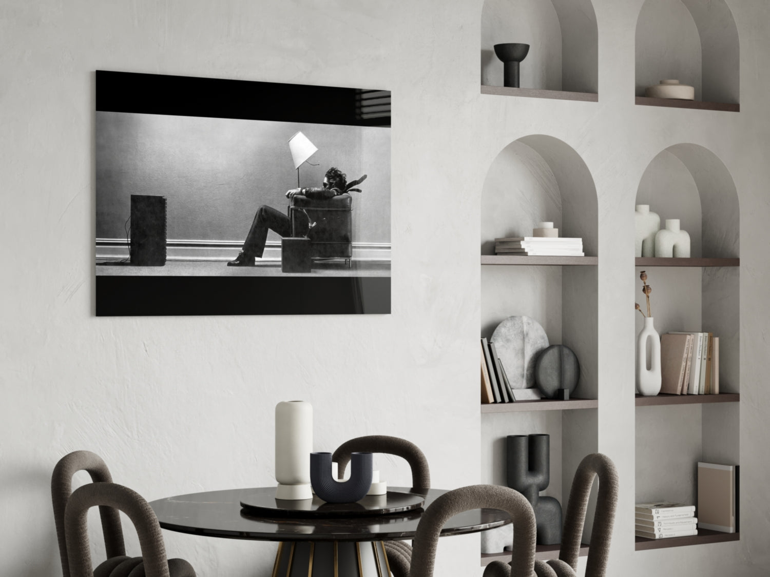 Black and white framed glass wall art depicting a figure sitting in a chair under a lamp, displayed above a dining table in a modern interior.