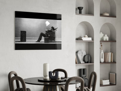 Black and white framed glass wall art depicting a figure sitting in a chair under a lamp, displayed above a dining table in a modern interior.