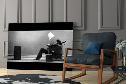 Black and white glass wall art depicting a silhouetted figure sitting in a chair with a lamp, displayed in a modern living room setting.