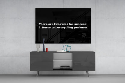 Black glass wall art displaying white text "There are two rules for success: 1. Never tell everything you know" mounted above gray media console.