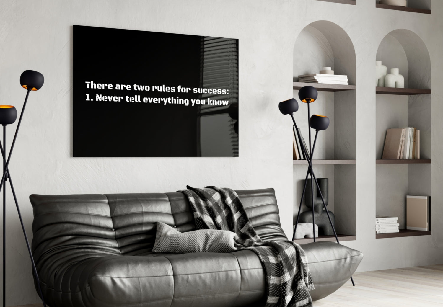 Black glass wall art with white text reading "There are two rules for success: 1. Never tell everything you know" displayed above a gray leather sofa in a modern living room.