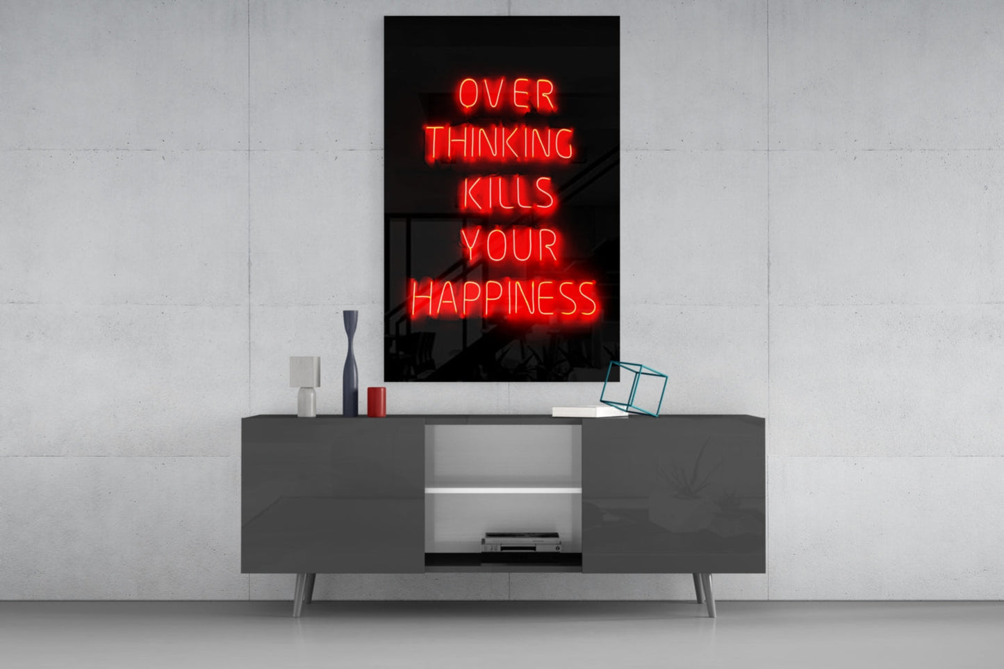 Red neon "OVER THINKING KILLS YOUR HAPPINESS" sign displayed on black glass above modern gray media console with decorative items.