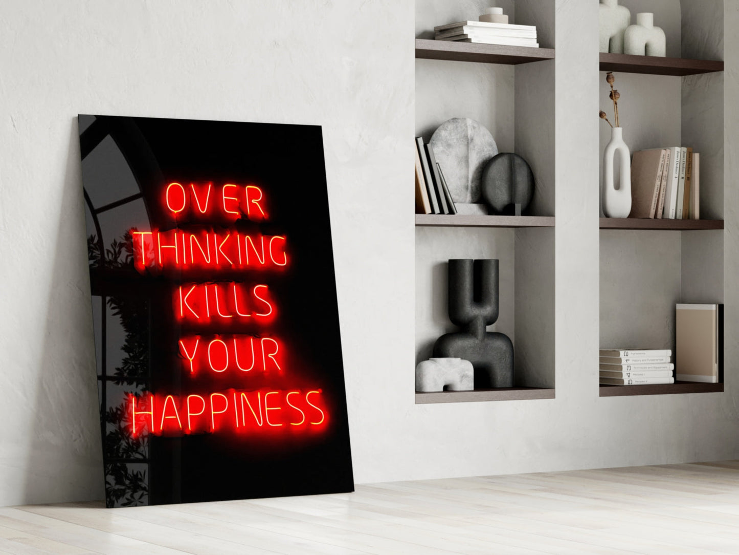 Red neon "Over Thinking Kills Your Happiness" text on black glass panel leaning against white wall with shelving.