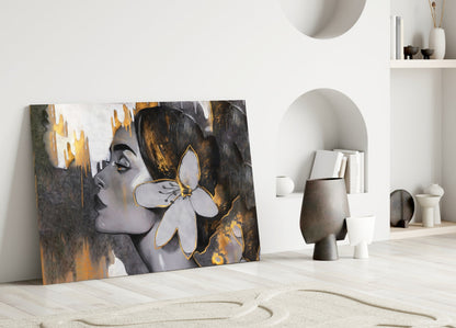 Glass wall art leaning against white wall showing woman's profile with golden flower and dark brushstrokes on white background.
