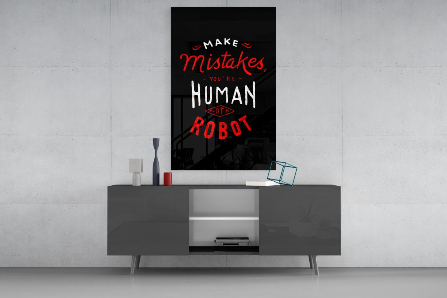 Black glass wall art with red and white text reading "Make Mistakes You're Human Not A Robot" displayed above a dark gray media console.
