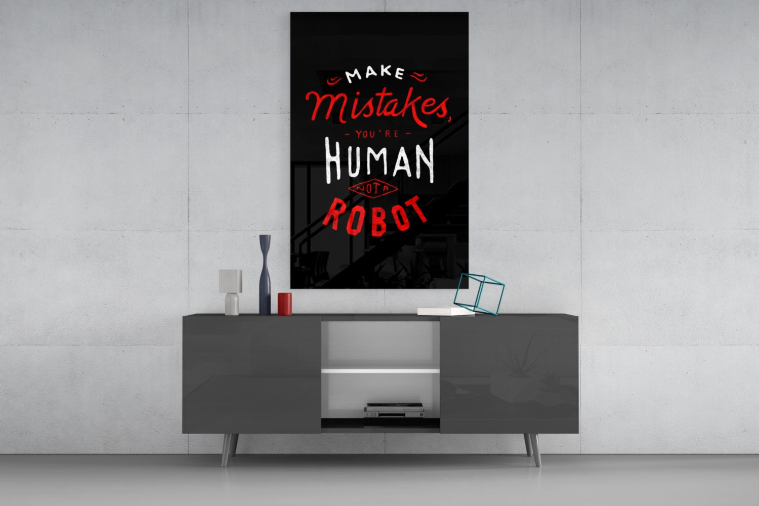Black glass wall art with red and white text reading "Make Mistakes You're Human Not A Robot" displayed above a dark gray media console.