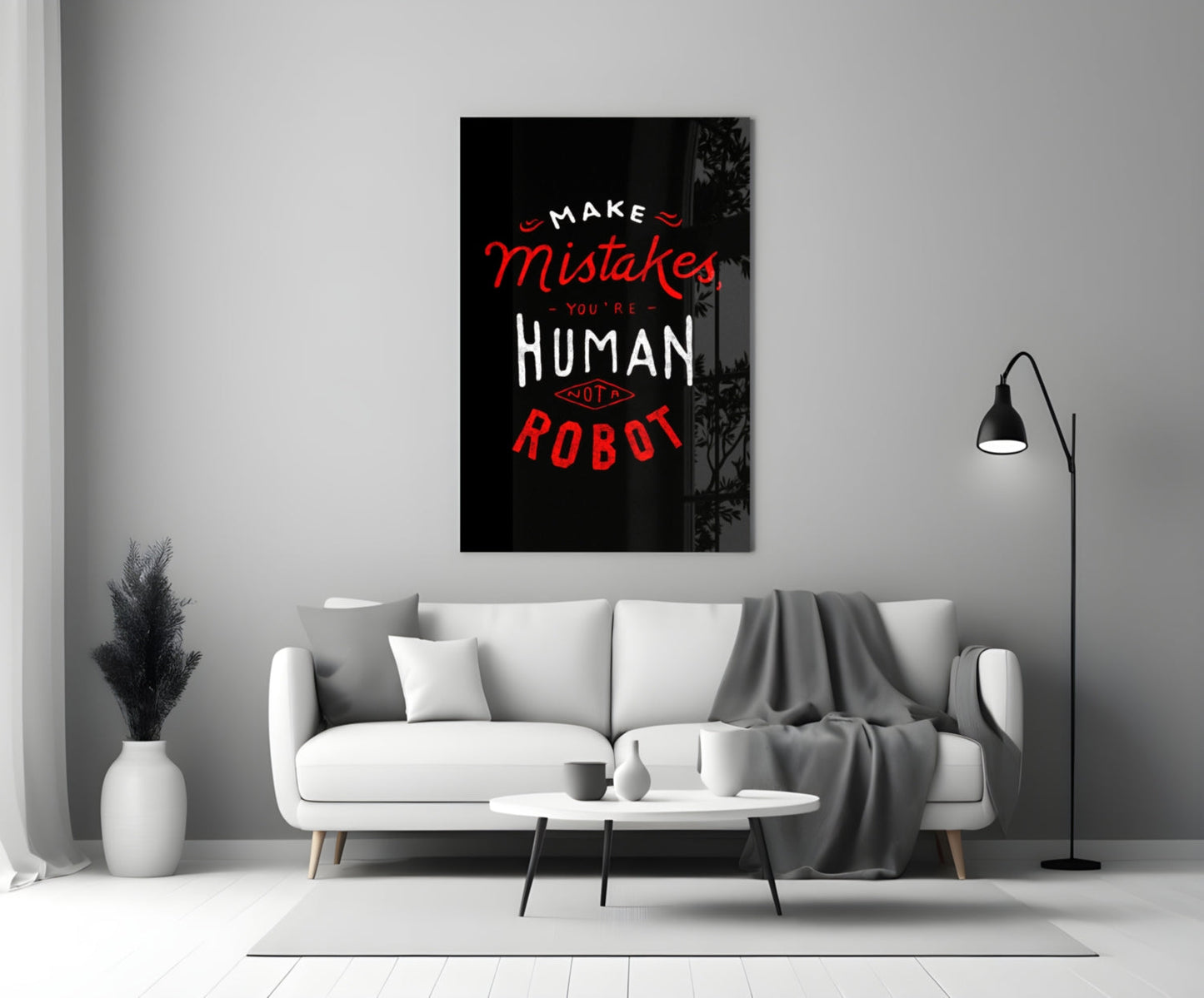 Black glass wall art with red and white text reading "Make Mistakes You're Human Not a Robot" displayed above a white sofa in a modern living room.