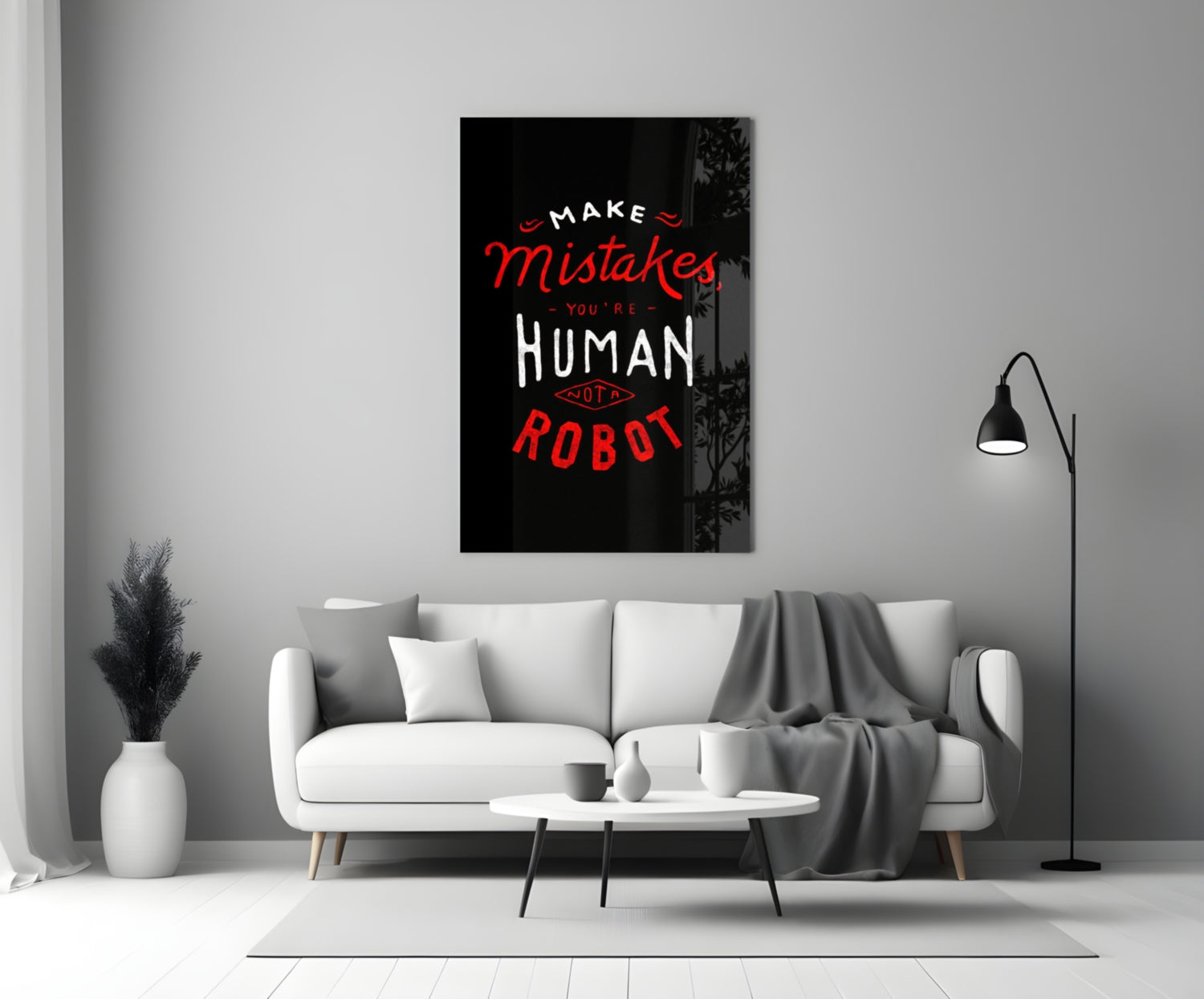 Black glass wall art with red and white text reading "Make Mistakes You're Human Not a Robot" displayed above a white sofa in a modern living room.
