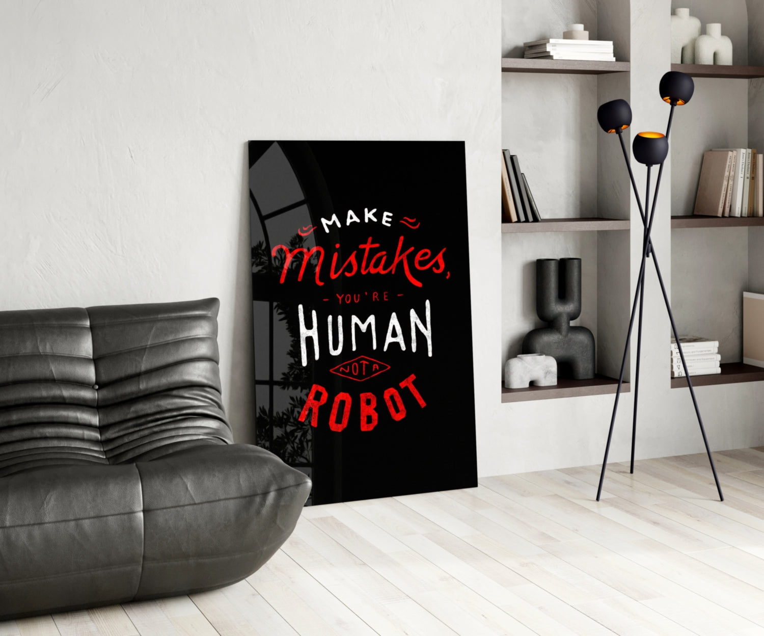 Black glass wall art with red and white text reading "Make Mistakes, You're Human Not a Robot" displayed in modern living room next to gray sofa.