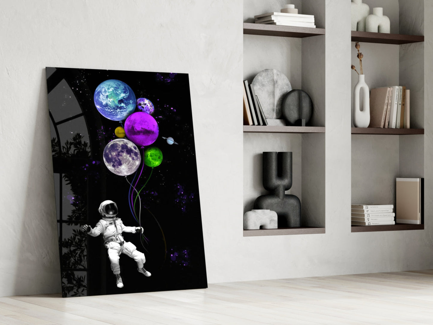 Astronaut holding colorful planet balloons against black starry background glass wall art leaning against white wall beside shelving.