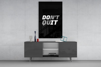 Modern minimalist living room with "Don't Quit" motivational text displayed on black glass wall art above dark grey media console.