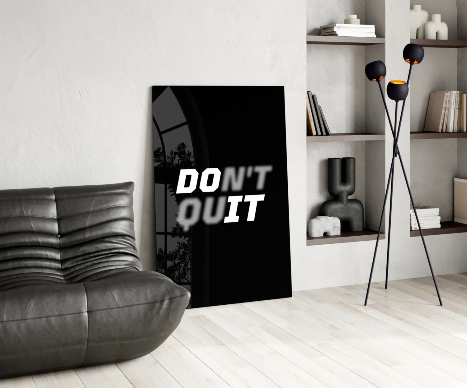 Black glass wall art displaying "DON'T QUIT" in white text, displayed in modern living room with gray sofa and shelving.