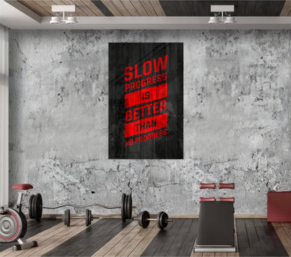 Modern gym interior with concrete wall displaying red and black glass art reading "Slow Progress is Better Than No Progress" above exercise equipment.