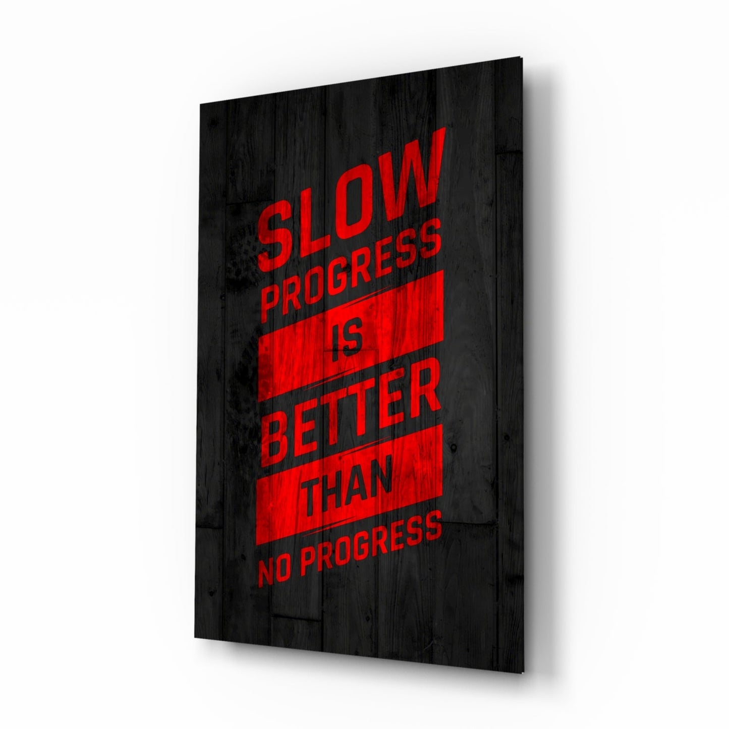 Angled perspective view of black wood-textured glass wall art displaying red text reading "Slow Progress Is Better Than No Progress.